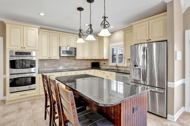 kitchen featuring stainless steel appliances, decorative backsplash, cream cabinets, a sink, and dark stone countertops