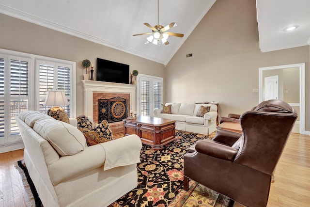 living area with light wood-style floors, a brick fireplace, crown molding, and high vaulted ceiling