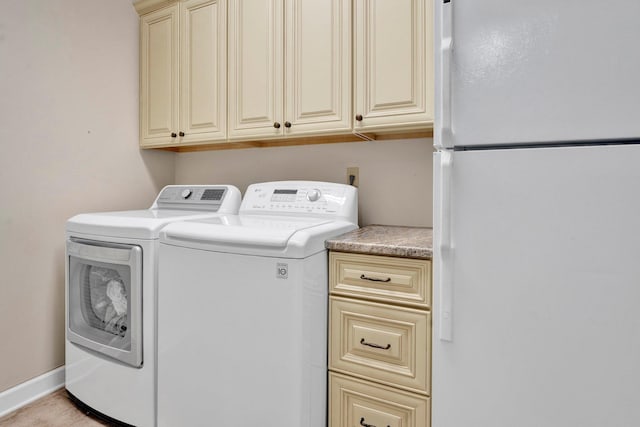 clothes washing area with cabinet space, baseboards, and washing machine and clothes dryer