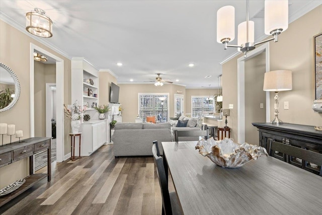 dining space with recessed lighting, built in features, dark wood-style flooring, crown molding, and ceiling fan with notable chandelier