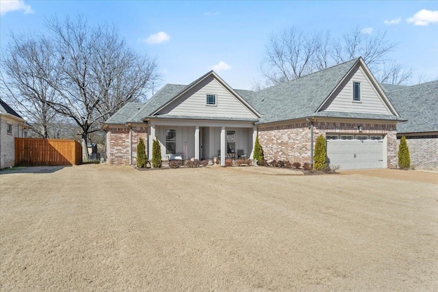 view of front facade featuring a porch, brick siding, driveway, and fence