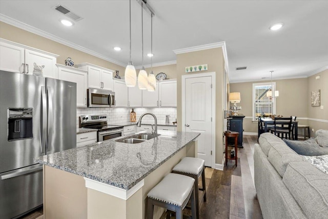 kitchen featuring visible vents, appliances with stainless steel finishes, ornamental molding, a sink, and a kitchen breakfast bar