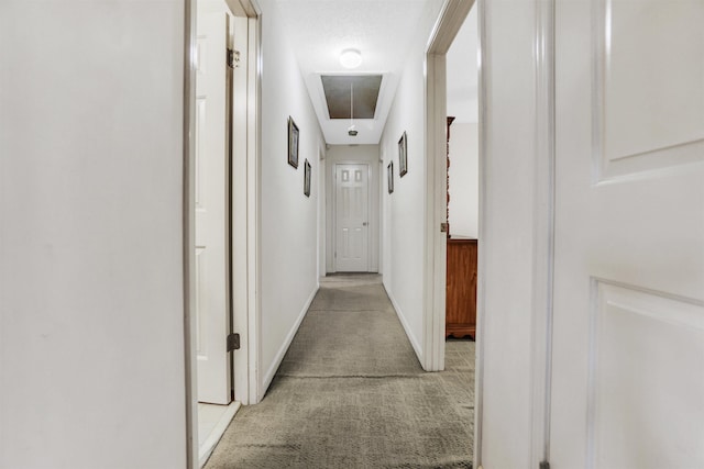 hallway featuring light carpet, attic access, and baseboards