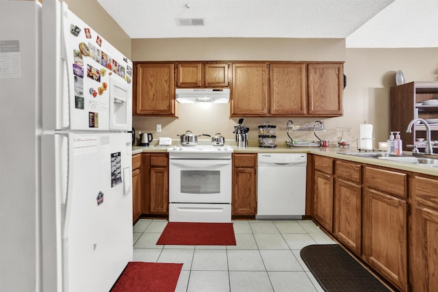 kitchen featuring white appliances, visible vents, brown cabinetry, under cabinet range hood, and a sink