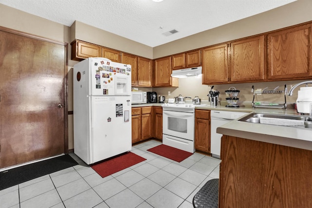 kitchen featuring under cabinet range hood, white appliances, a sink, light countertops, and brown cabinetry