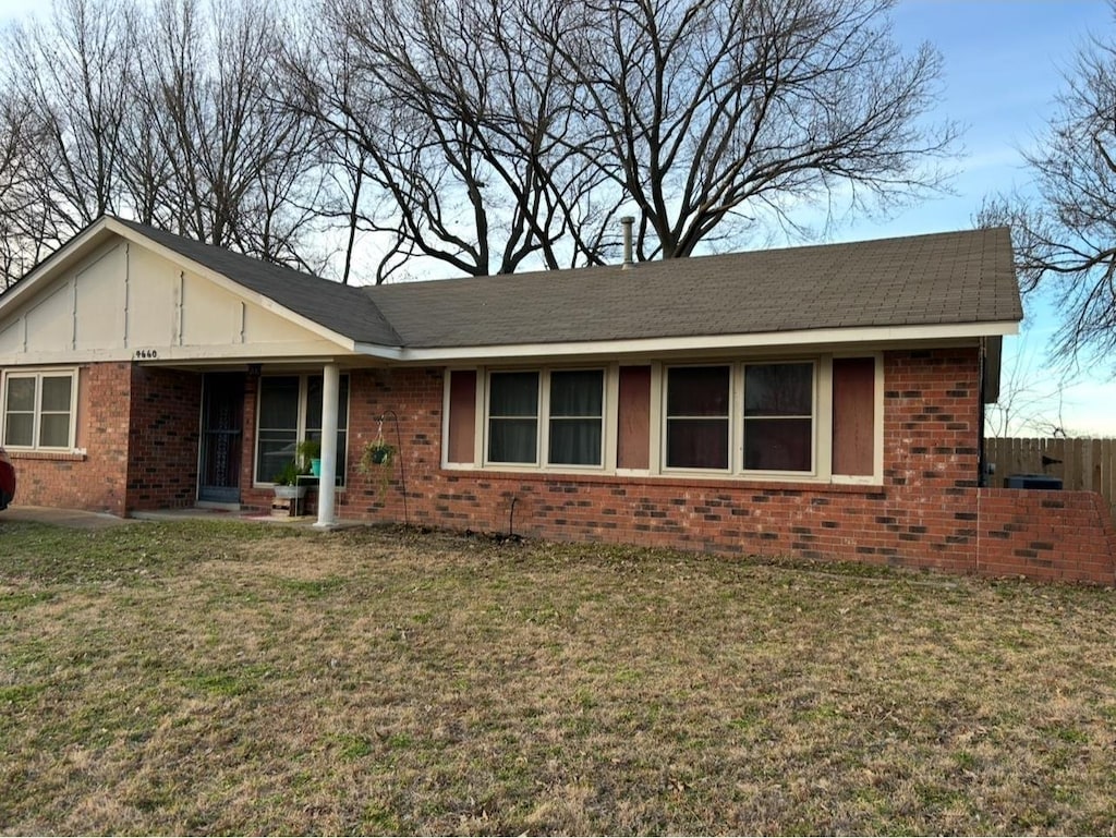 ranch-style house featuring brick siding, board and batten siding, a front yard, and fence