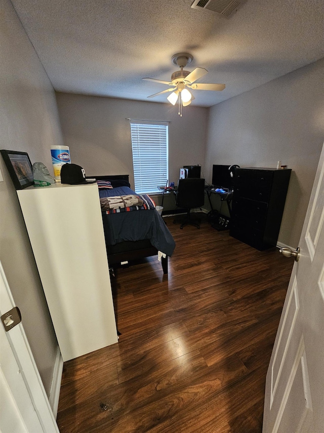 bedroom with ceiling fan, a textured ceiling, visible vents, and wood finished floors