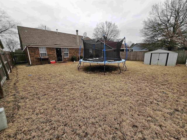 rear view of property featuring a fenced backyard, brick siding, an outdoor structure, a storage unit, and a trampoline