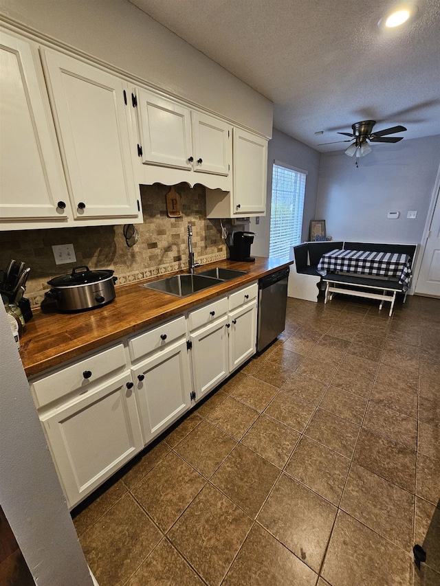 kitchen with a sink, white cabinets, wooden counters, stainless steel dishwasher, and backsplash