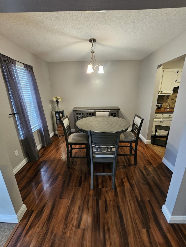 dining area featuring dark wood-style floors, a notable chandelier, a textured ceiling, and baseboards