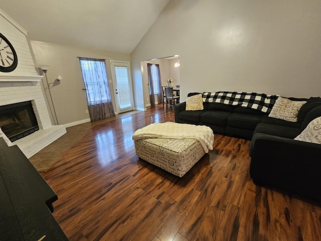 living area featuring high vaulted ceiling, a brick fireplace, wood finished floors, and baseboards