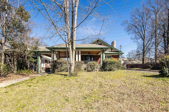 view of front of house with covered porch, a chimney, brick siding, and a front yard