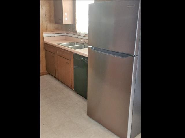 kitchen with black dishwasher, light floors, light countertops, freestanding refrigerator, and a sink