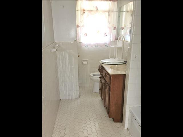 bathroom featuring toilet, tile patterned flooring, tile walls, and vanity