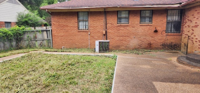 view of side of home featuring roof with shingles, a yard, brick siding, central AC, and fence