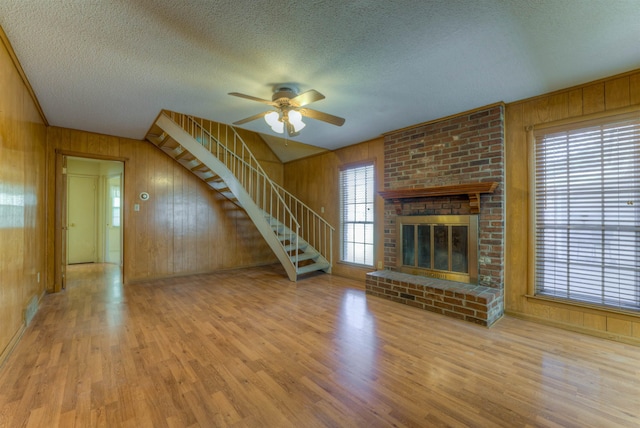 unfurnished living room featuring wood walls, stairway, a fireplace, and wood finished floors