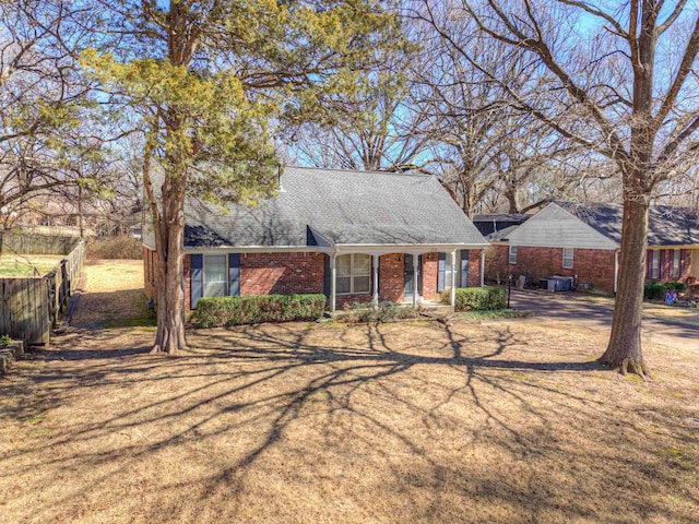 view of front of home with brick siding, a shingled roof, fence, and a front yard