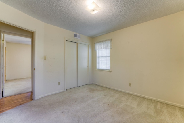 unfurnished bedroom featuring baseboards, visible vents, a textured ceiling, carpet flooring, and a closet