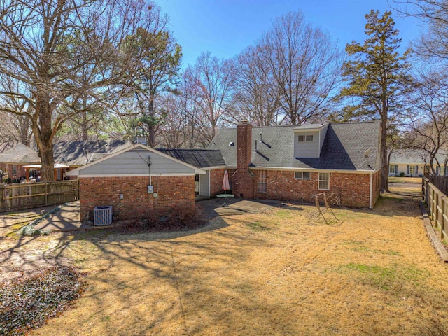 rear view of property featuring brick siding, fence, a chimney, and a lawn