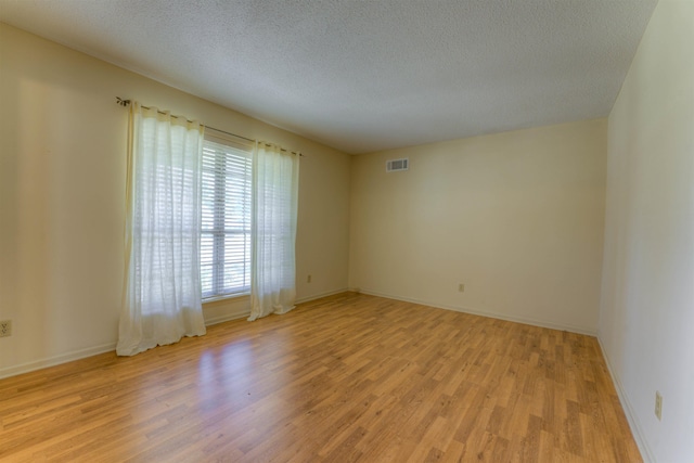 empty room featuring baseboards, visible vents, light wood-style flooring, and a textured ceiling