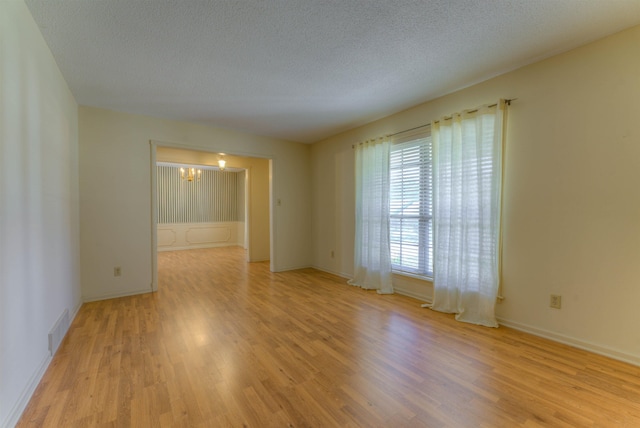 unfurnished room with a chandelier, visible vents, light wood-style floors, and a textured ceiling