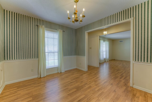 empty room featuring visible vents, an inviting chandelier, a textured ceiling, wood finished floors, and wallpapered walls