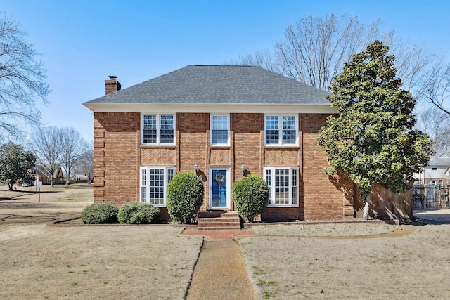 colonial home with a shingled roof, brick siding, and a chimney