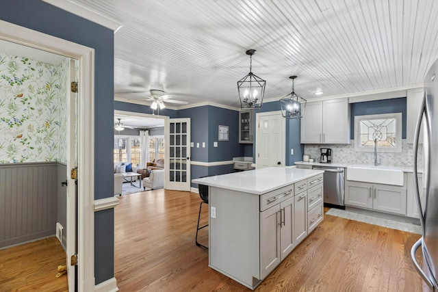 kitchen with a breakfast bar, a wainscoted wall, gray cabinets, appliances with stainless steel finishes, and a sink