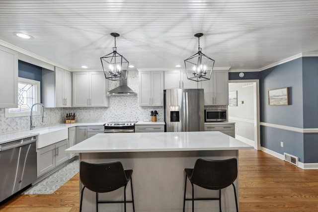 kitchen featuring visible vents, wall chimney exhaust hood, a breakfast bar, stainless steel appliances, and a sink