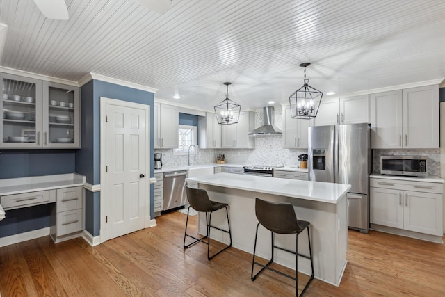 kitchen with stainless steel appliances, wall chimney range hood, a center island, light wood finished floors, and a kitchen bar