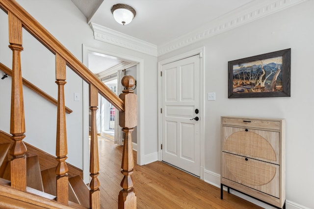 foyer featuring light wood-style floors, ornamental molding, baseboards, and stairs