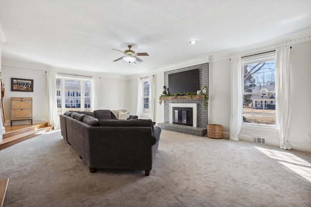 living area with ceiling fan, visible vents, ornamental molding, a brick fireplace, and carpet