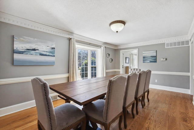 dining area with baseboards, visible vents, crown molding, a textured ceiling, and light wood-style floors