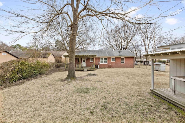 back of property featuring a wooden deck, a lawn, and brick siding