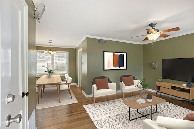 living area featuring ornamental molding, ceiling fan with notable chandelier, baseboards, and wood finished floors