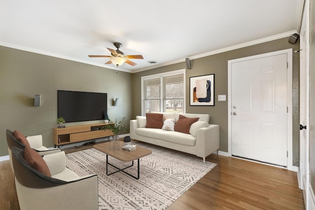 living area featuring ceiling fan, ornamental molding, wood finished floors, and baseboards