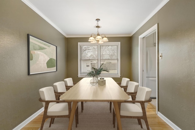 dining room featuring light wood finished floors, baseboards, ornamental molding, and an inviting chandelier