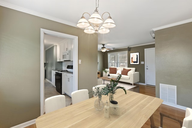 dining space featuring crown molding, visible vents, wood finished floors, baseboards, and ceiling fan with notable chandelier