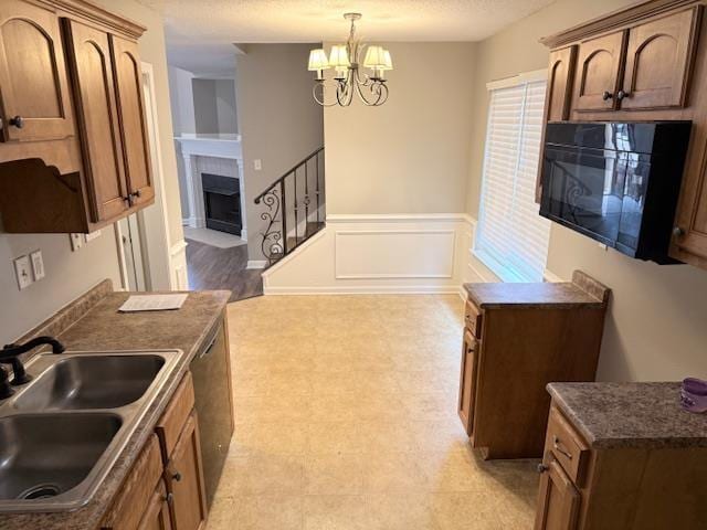 kitchen with dark countertops, a fireplace with flush hearth, a sink, a decorative wall, and stainless steel dishwasher