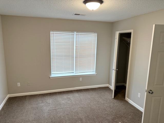 unfurnished bedroom with baseboards, visible vents, dark colored carpet, and a textured ceiling