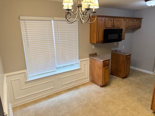 kitchen featuring black microwave, a chandelier, a decorative wall, a wainscoted wall, and brown cabinets