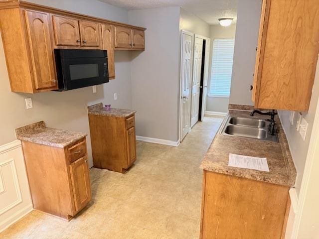 kitchen featuring baseboards, brown cabinetry, light countertops, black microwave, and a sink