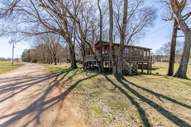 exterior space featuring a deck, dirt driveway, stairway, and a front yard