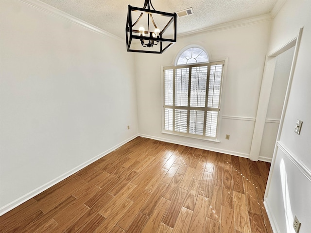 unfurnished dining area featuring ornamental molding, a textured ceiling, wood finished floors, a chandelier, and baseboards