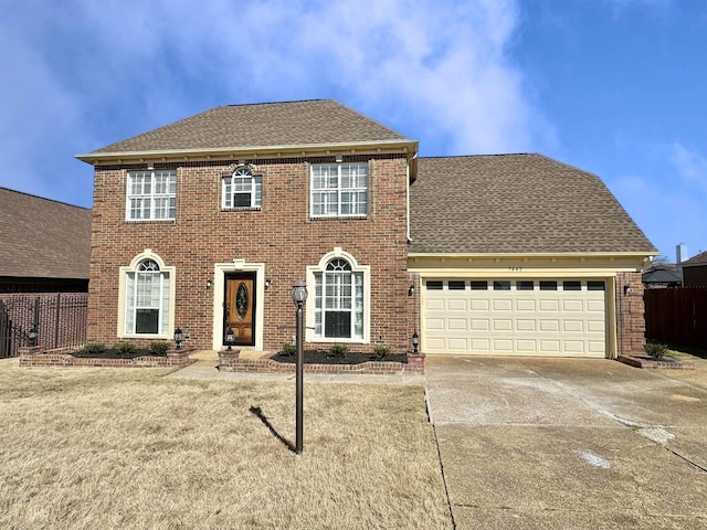 colonial home featuring roof with shingles, brick siding, fence, a garage, and driveway