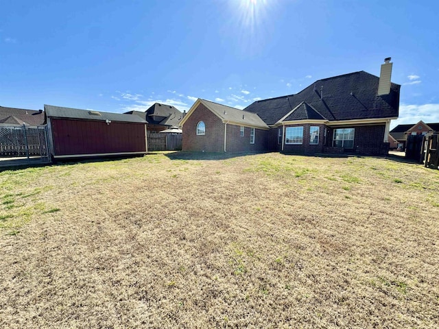 rear view of property with brick siding, a chimney, fence, and a yard