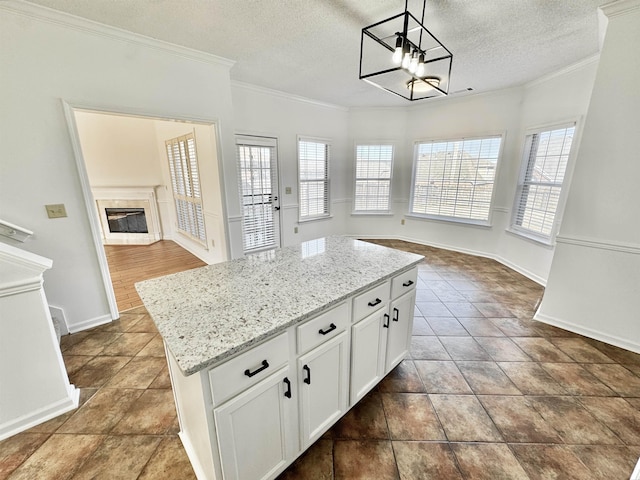 kitchen featuring a glass covered fireplace, open floor plan, a center island, light stone countertops, and crown molding