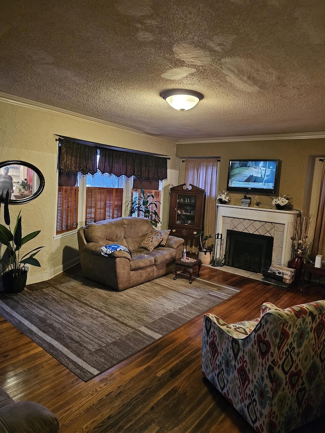 living room featuring a textured wall, ornamental molding, a textured ceiling, wood finished floors, and a tile fireplace