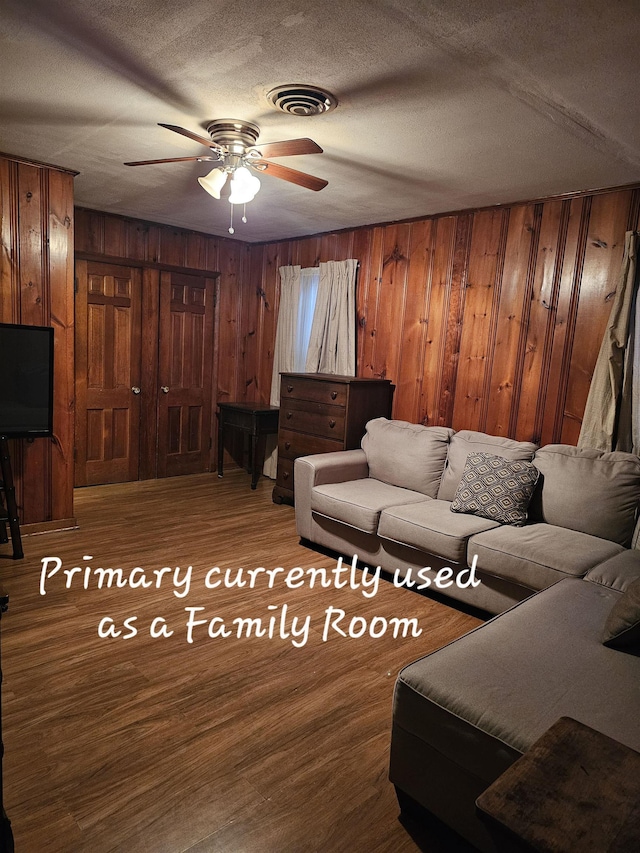 living area featuring a textured ceiling, ceiling fan, wood walls, wood finished floors, and visible vents