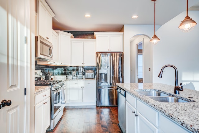 kitchen featuring appliances with stainless steel finishes, dark wood-style flooring, hanging light fixtures, a sink, and backsplash